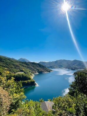 A panoramic view of a lake surrounded by hills, with a clear sky and sunlight.