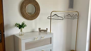 A room with a white dresser, a mirror, a gold hanger rack, and a bed with a textured white bedspread.