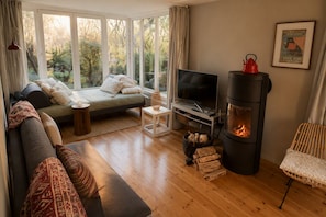 A cozy living room with a sofa, TV, fireplace, and a view of the outdoors. - A Swedish-style house with a sunny, wooded garden, near Lakes Stechlin and Dagow. (Stechlin)