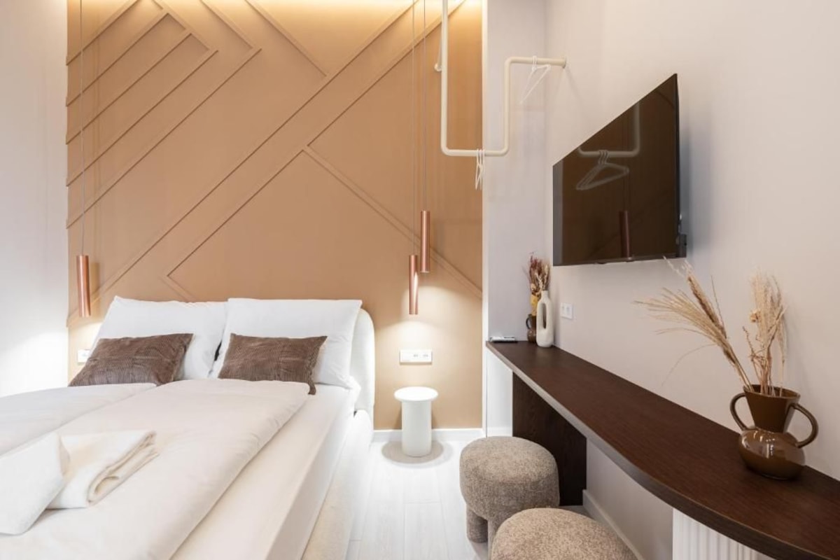 Ein modernes Hotelzimmer mit Bett, Nachttisch, Wand-Fernseher und einem kleinen Beistelltisch.