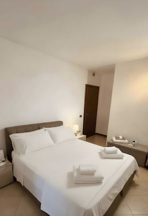 Ein Hotelzimmer mit einem großen Bett, einem Nachttisch mit Lampe, einer Tür und einem kleinen Tisch mit Handtüchern.
