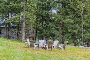 A grassy outdoor area with Adirondack chairs arranged around a table, surrounded by trees. - Lakeview Retreat | Theater, Games & 140 Acres (Monticello)