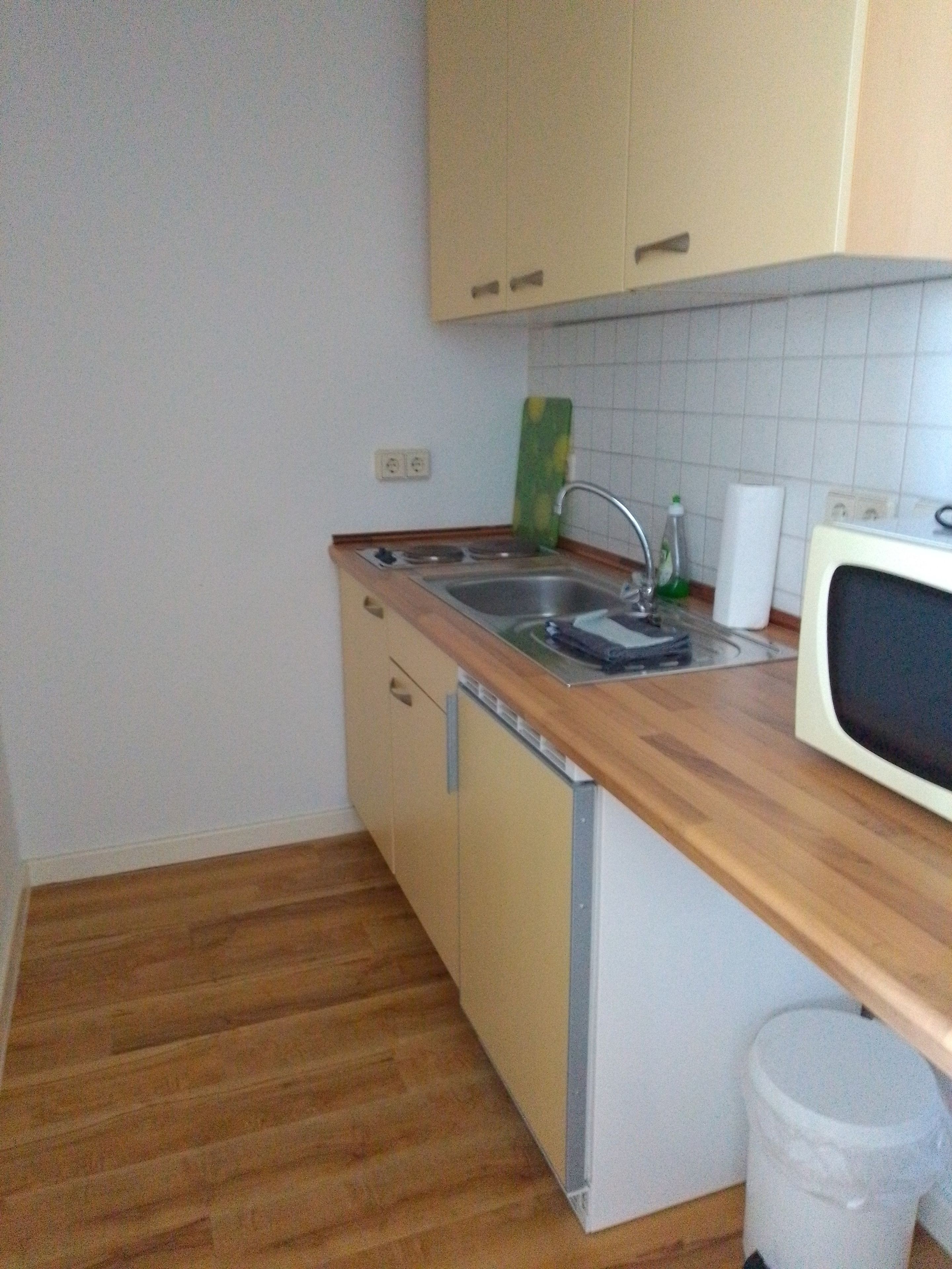 Eine kleine Küche mit einer Holzausziehtafel, einem Spülbecken, einer Mikrowelle und einem Mülleimer.