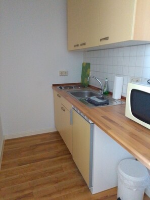 Eine kleine Küche mit einer Holzausziehtafel, einem Spülbecken, einer Mikrowelle und einem Mülleimer.
