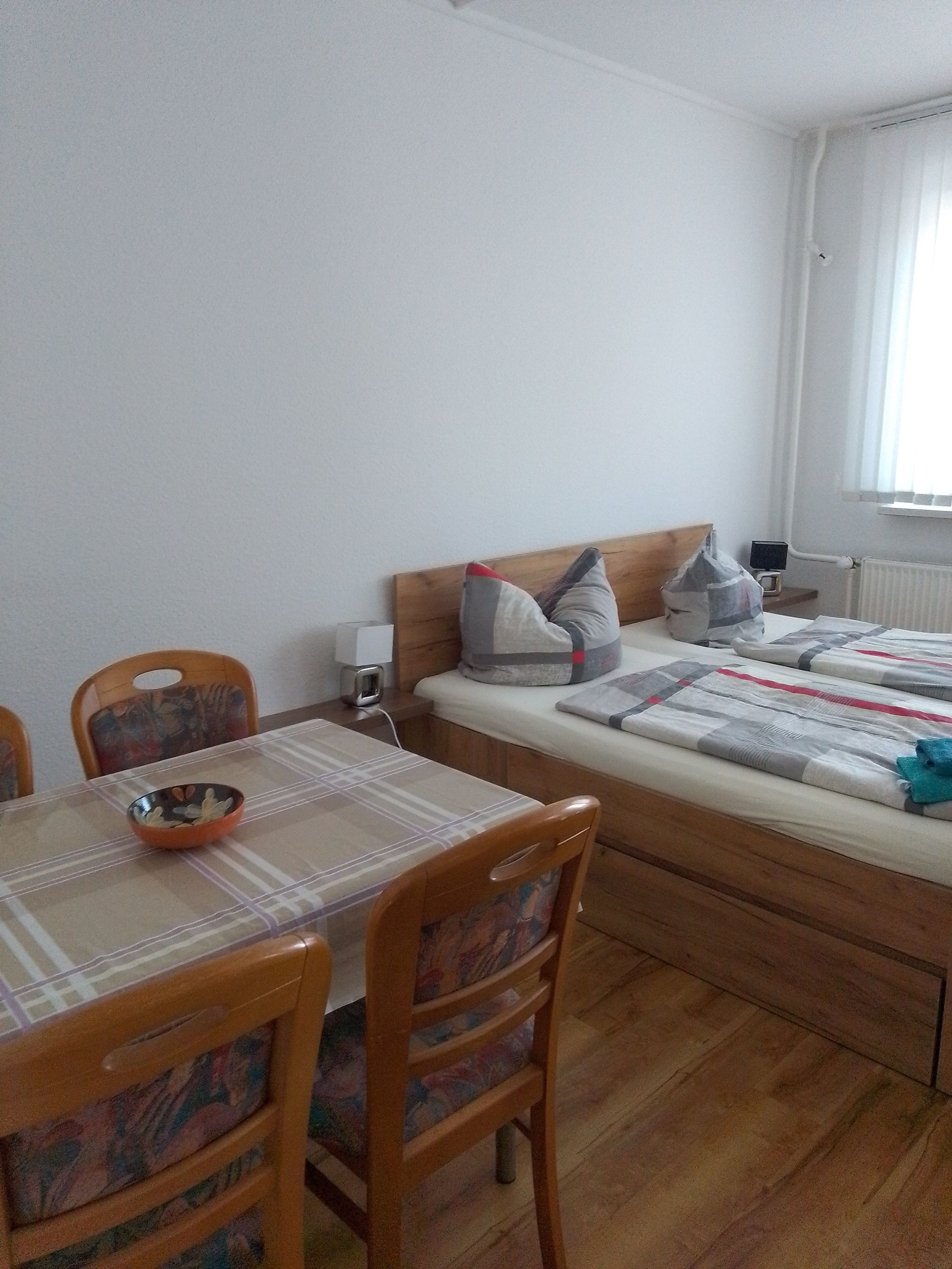 A room with a bed, a table with chairs, a bowl on the table, and a window with curtains.