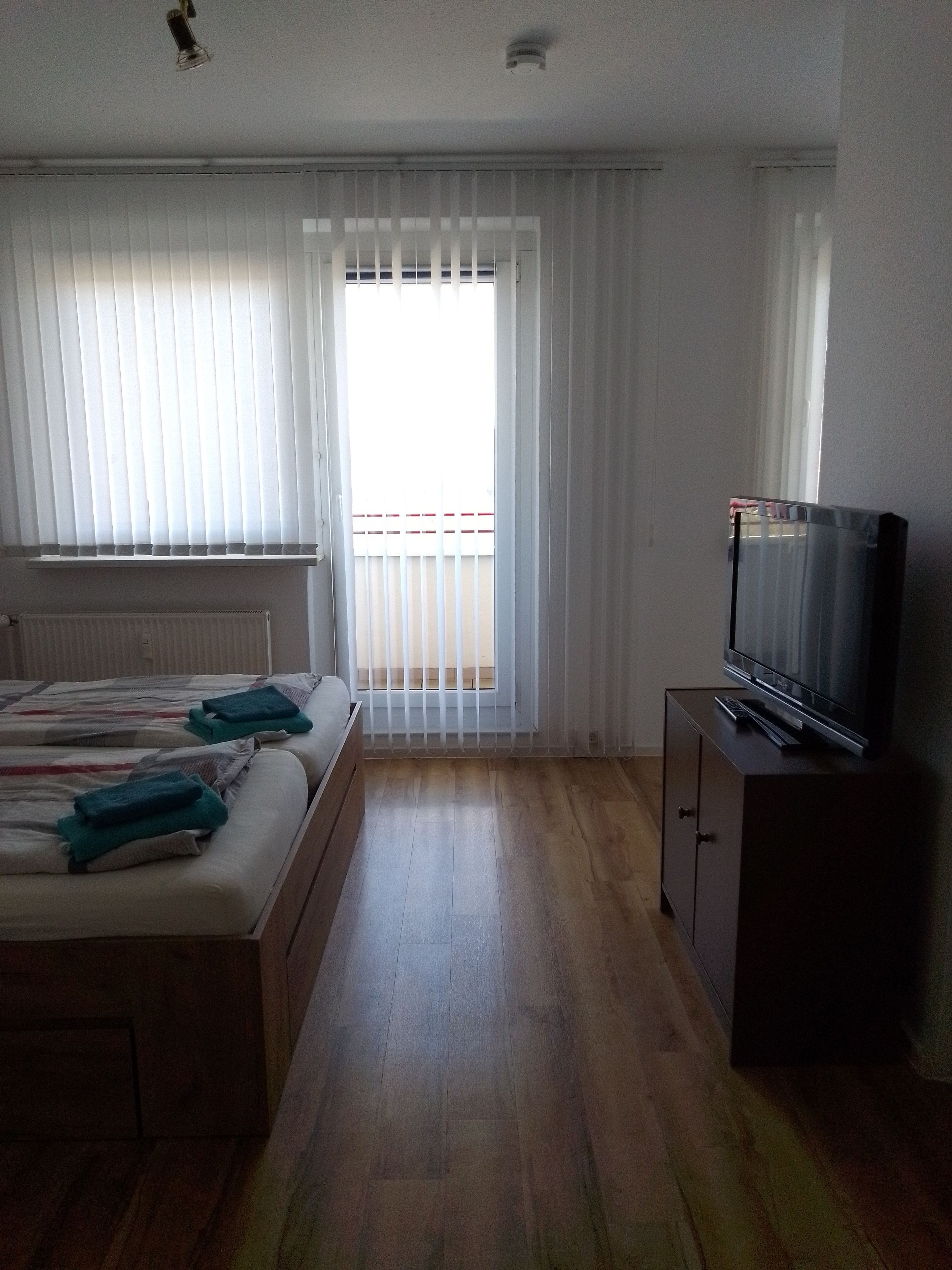 Ein Zimmer mit zwei Betten, einem Fernseher auf einer Kommode und einem Fenster mit Jalousien.