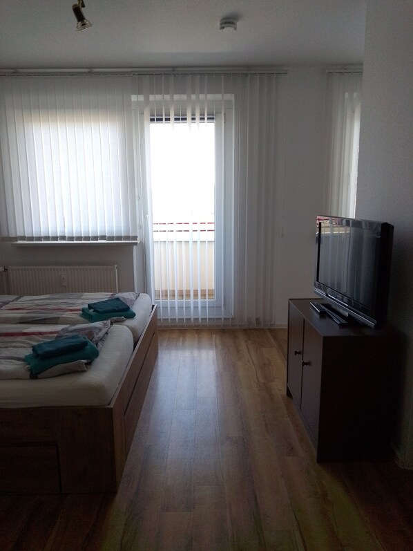 A room with two beds, a television on a cabinet, and a window with blinds.