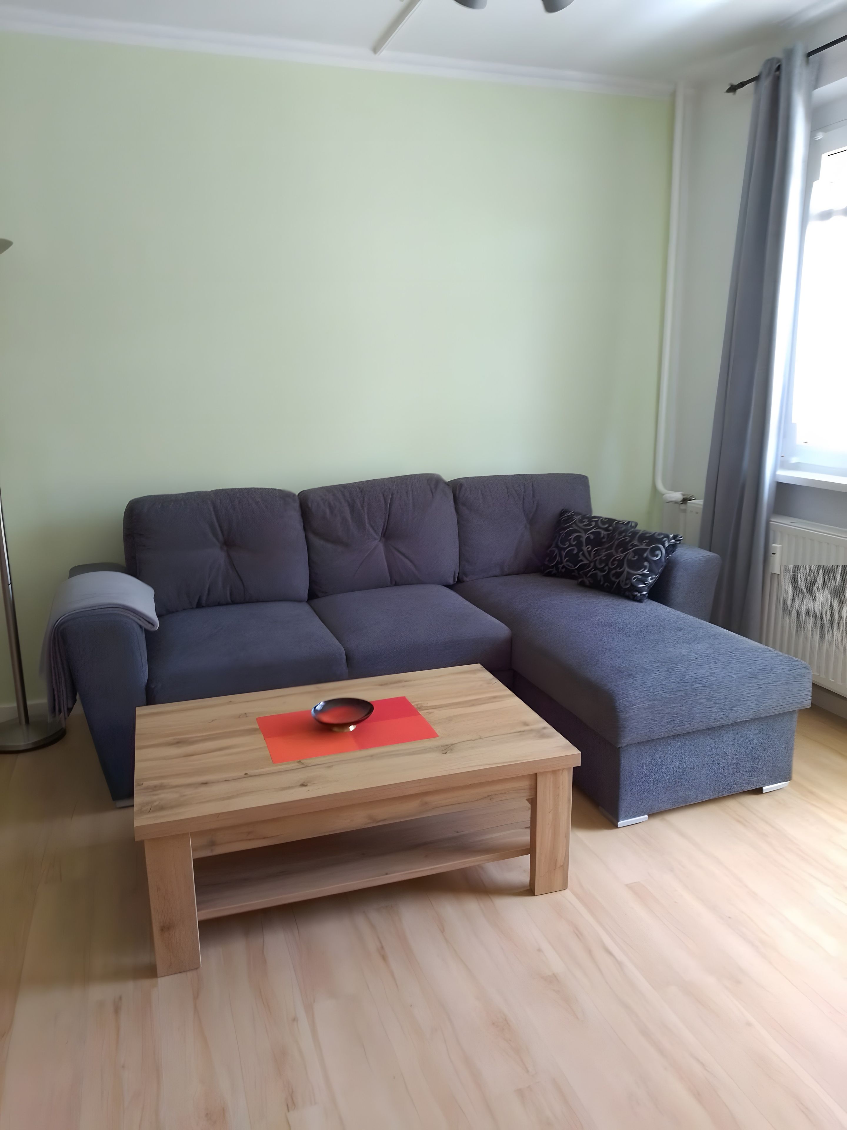 A modern living room with a sectional sofa, a wooden coffee table, and a radiator.