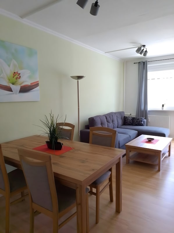 A living room with a sofa, a dining table with chairs, a floor lamp, and a painting on the wall.