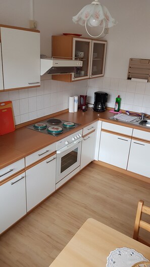 Una cocina con armarios blancos, encimera de madera, estufa y cafetera.