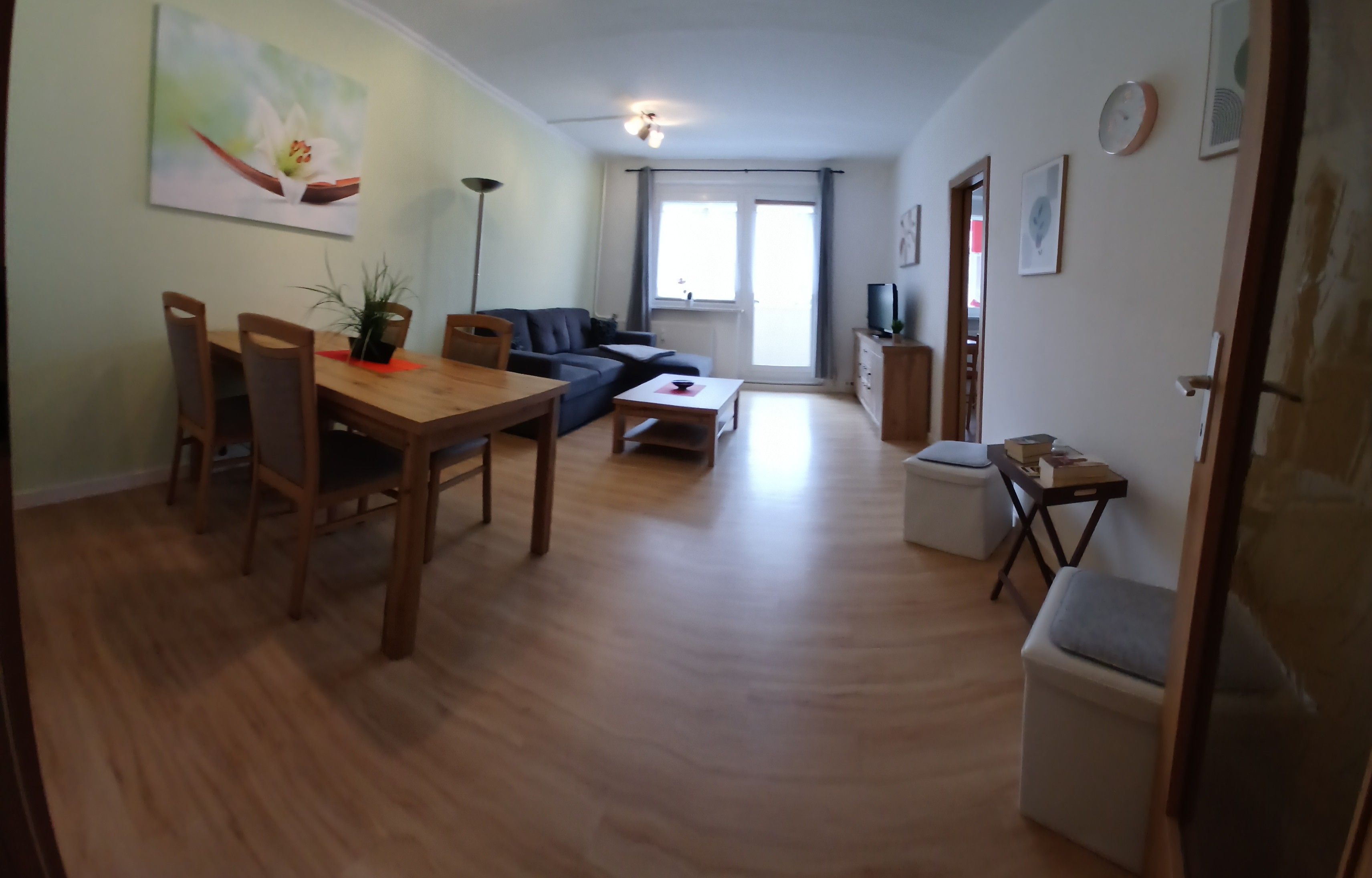 A living room with a sofa, a dining table, chairs, a coffee table, a TV, and a small cabinet.