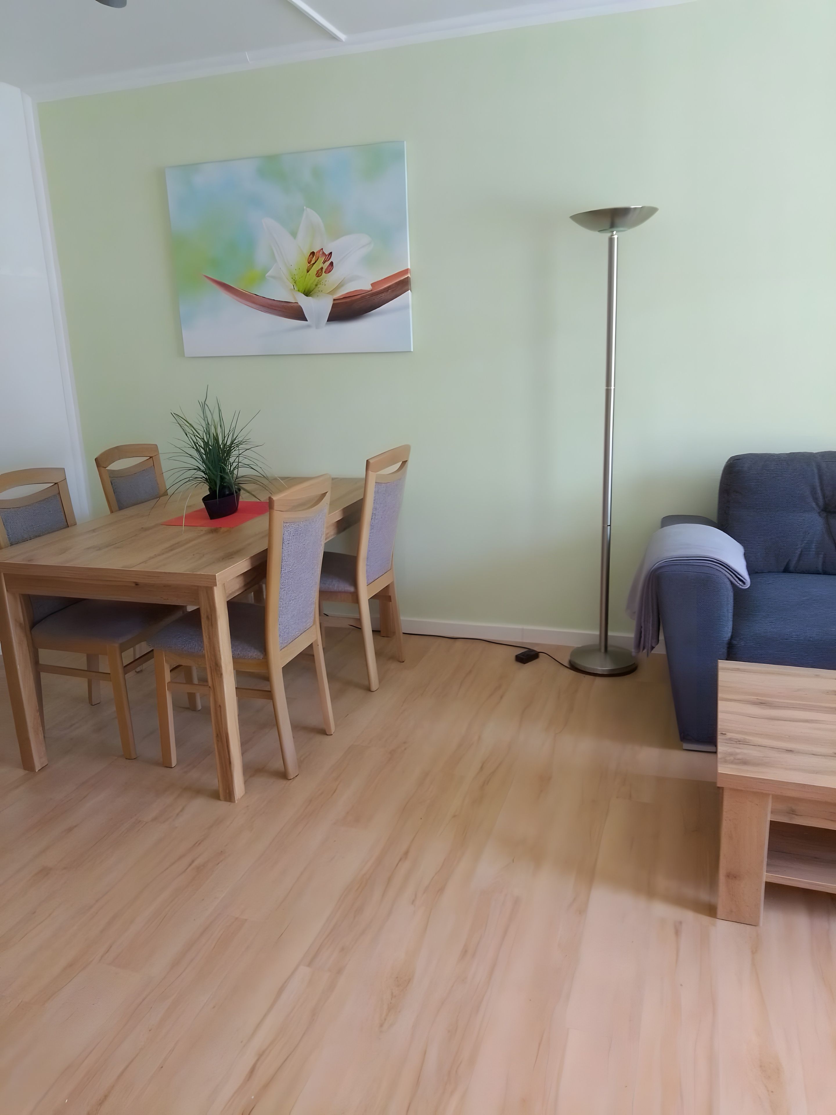 A dining area with a wooden table and chairs, a potted plant, and a painting on the wall.