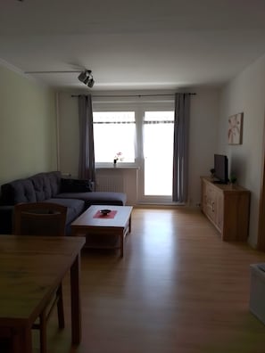 Una sala de estar con sofá, mesa de centro, televisor sobre un mueble bajo y ventilador de techo.