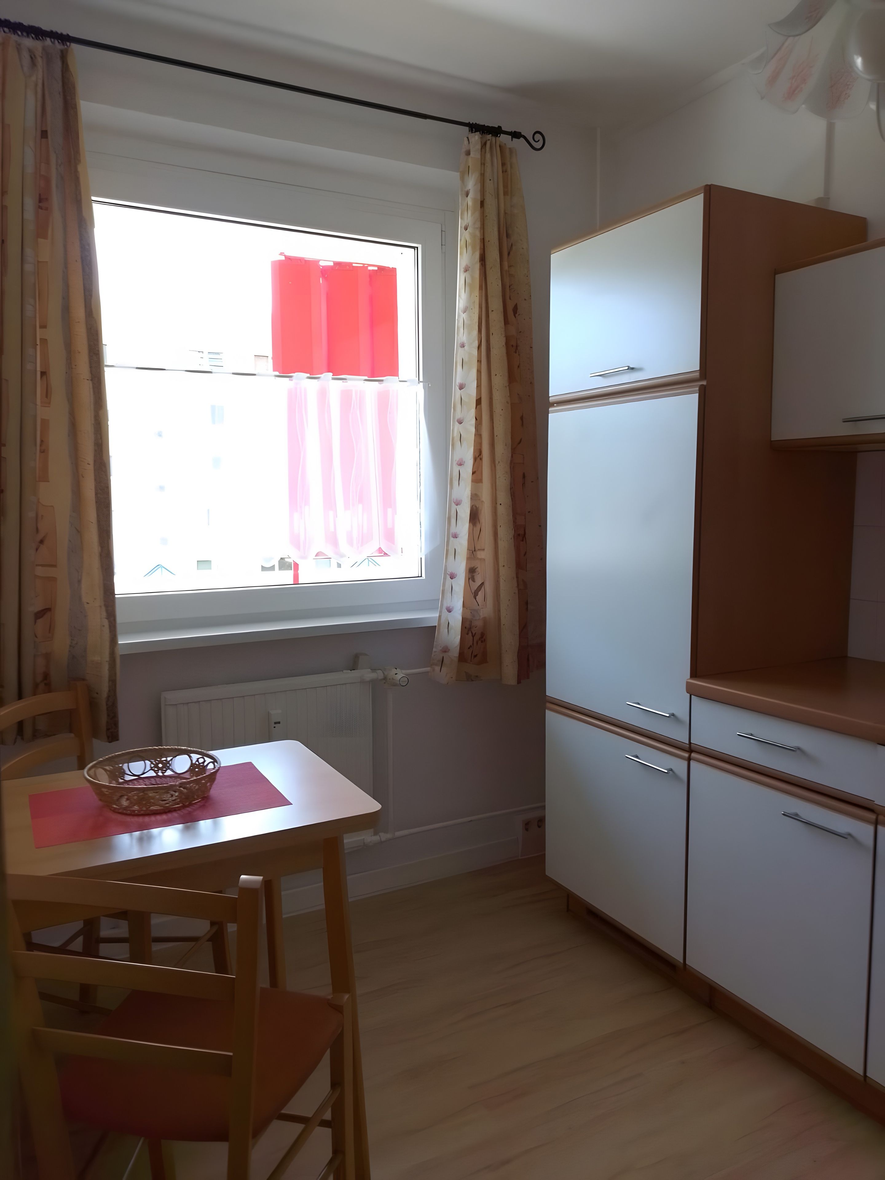 A kitchen with a window, a table with chairs, and a refrigerator.