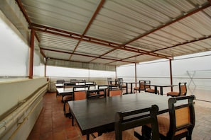 An indoor dining area with tables and chairs, a tiled floor, and a metal roof structure. - Hotel O Manu Residency (Bangalore)