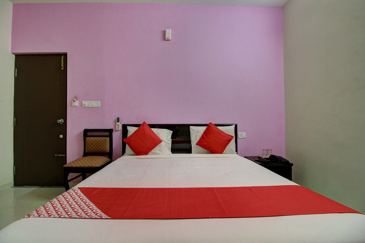 A hotel room with a bed, a chair, a nightstand, and a door.