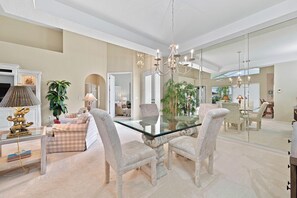 A spacious dining area with a glass table and white upholstered chairs, a chandelier, and a large mirror reflecting the room. - Lakeview home with Golf - 5 Minutes to Gulf Beaches (Bonita Springs)