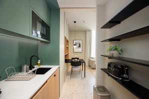 A compact kitchen with a microwave, sink, and a toaster. There is a dining area with a table and chairs, and a small plant on a shelf. - Chic Studio in Upside Living | Burj Khalifa View (Dubai)