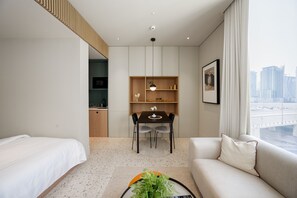 A hotel room with a bed, a sofa, a dining table with chairs, a small kitchen area, and a view of the city through the window. - Chic Studio in Upside Living | Burj Khalifa View (Dubai)
