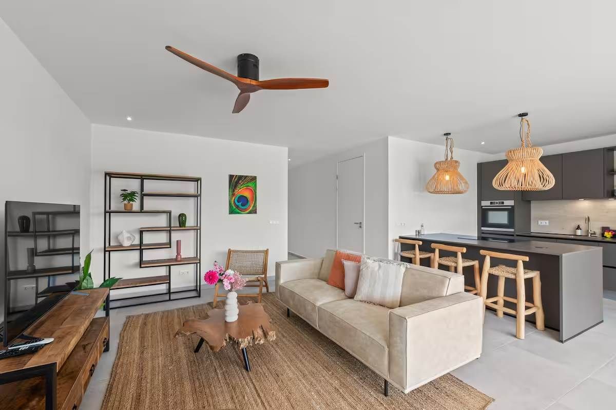 Een moderne woonkamer met een bank, salontafel en een eethoek met barstoelen.