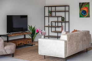 Een moderne woonkamer met een flatscreen televisie, een witte bank, een houten tv-meubel en een decoratieve plant.