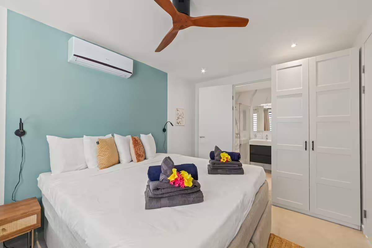Hotelkamer met een bed, een plafondventilator, een airconditioningapparaat, een kledingkast en een badkamer, zichtbaar door een geopende deur.