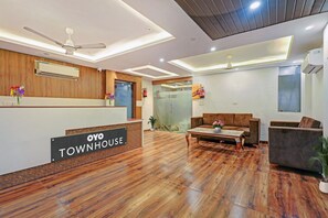 A reception area with a wooden reception desk labeled 'OYO TOWN HOUSE,' a seating area with sofas and a coffee table, and a glass partition. - Townhouse Lucky Grand Palace (Ghaziabad)