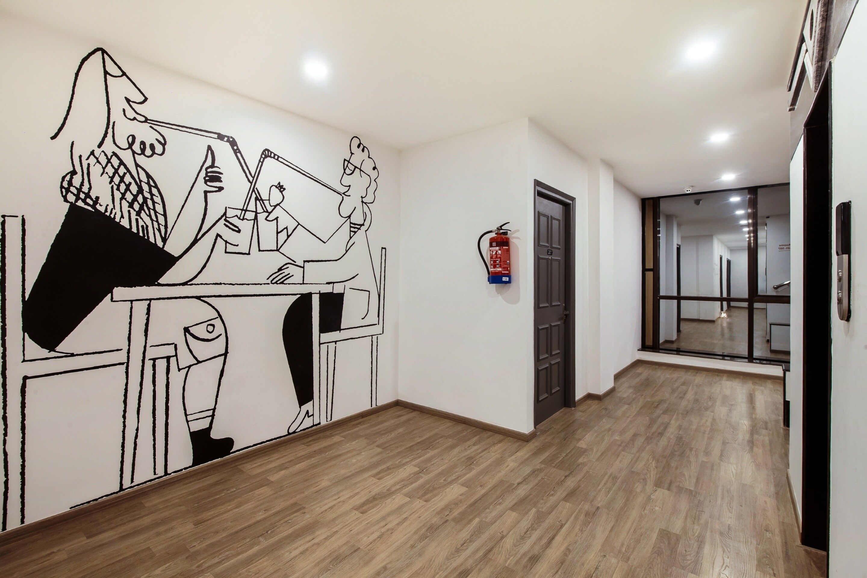 A hallway with a wooden floor, a fire extinguisher mounted on the wall, and a door leading to another room.