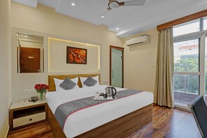 A hotel room with a large bed, a nightstand, a vase of red flowers, a painting on the wall, and a view through the window. - Townhouse Lucky Grand Palace (Ghaziabad)