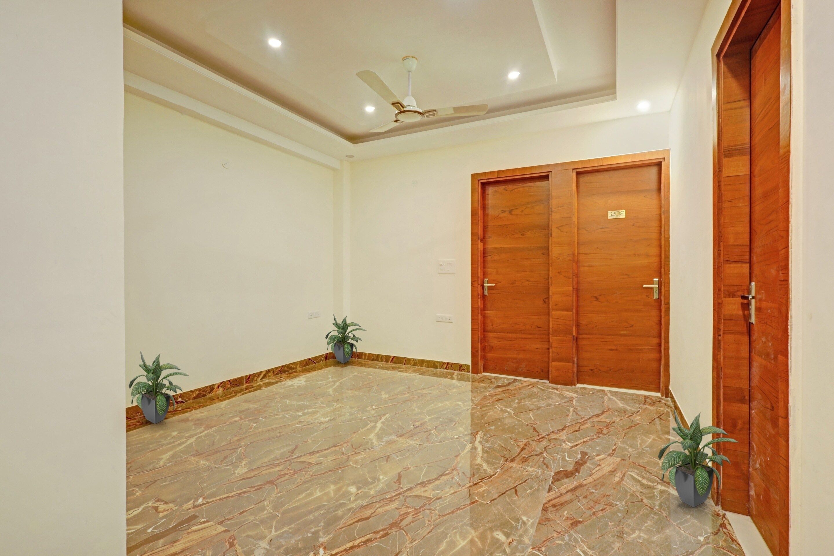 A room with a marble floor, two wooden doors, a ceiling fan, and two potted plants.