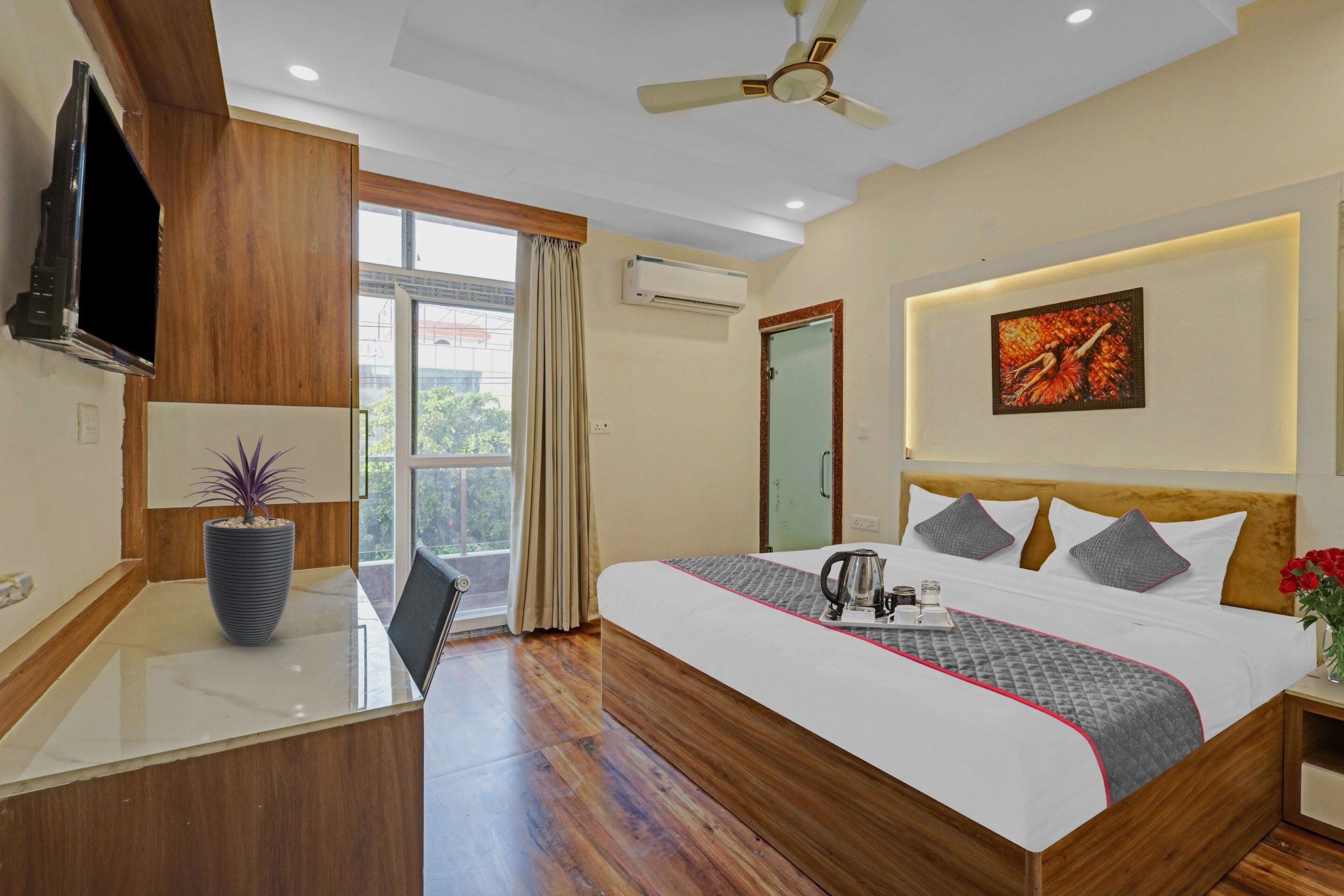 A hotel room with a bed, a desk, a chair, a TV, a ceiling fan, and a window with curtains.