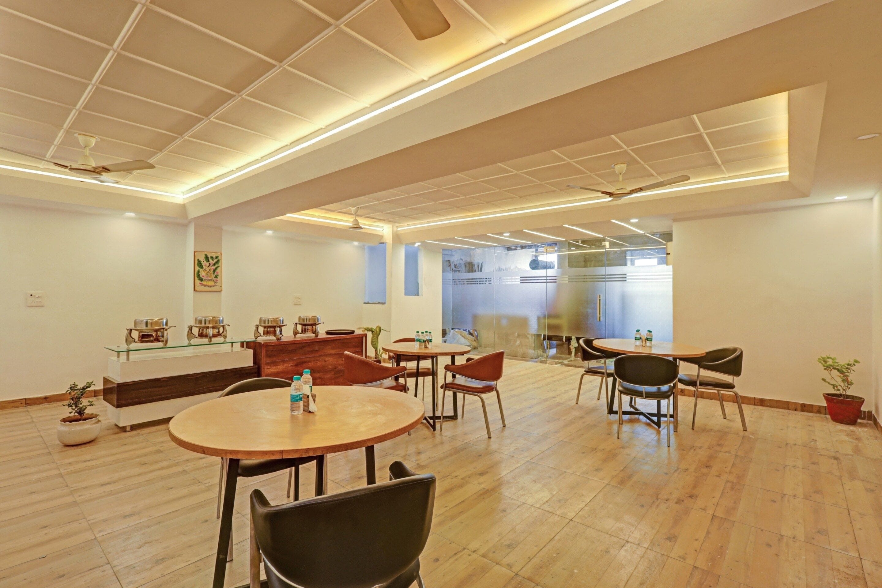 A modern dining area with round tables and chairs, a wooden floor, and ceiling fans.
