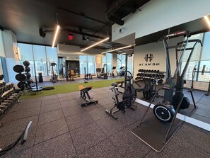A gym with various exercise equipment, a green exercise mat, and a wall with a logo. - NEW High-rise 1BR Den Rooftop Pool Gym 402 (Miami)