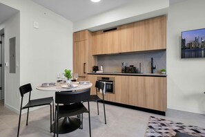 A modern kitchen with wooden cabinets, a built-in oven, and a dining area with a round table and chairs. - NEW High-rise 1BR Den Rooftop Pool Gym 402 (Miami)