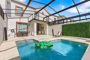 A swimming pool with a green inflatable turtle, a covered patio with chairs, and a green hedge wall. - NEW 4BR Private Pool Lazy River Themed Rooms (Kissimmee)