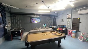 A pool table with a foosball table, a television, and a bicycle in a room with grey walls and a ceiling fan. - Coming Soon Solterra 5184 (Davenport)
