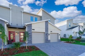 A modern residential building with a garage, a red door, and a well-maintained lawn. - NEW 2Bd Retreat With Game Room Lazy River 9333 (Davenport)