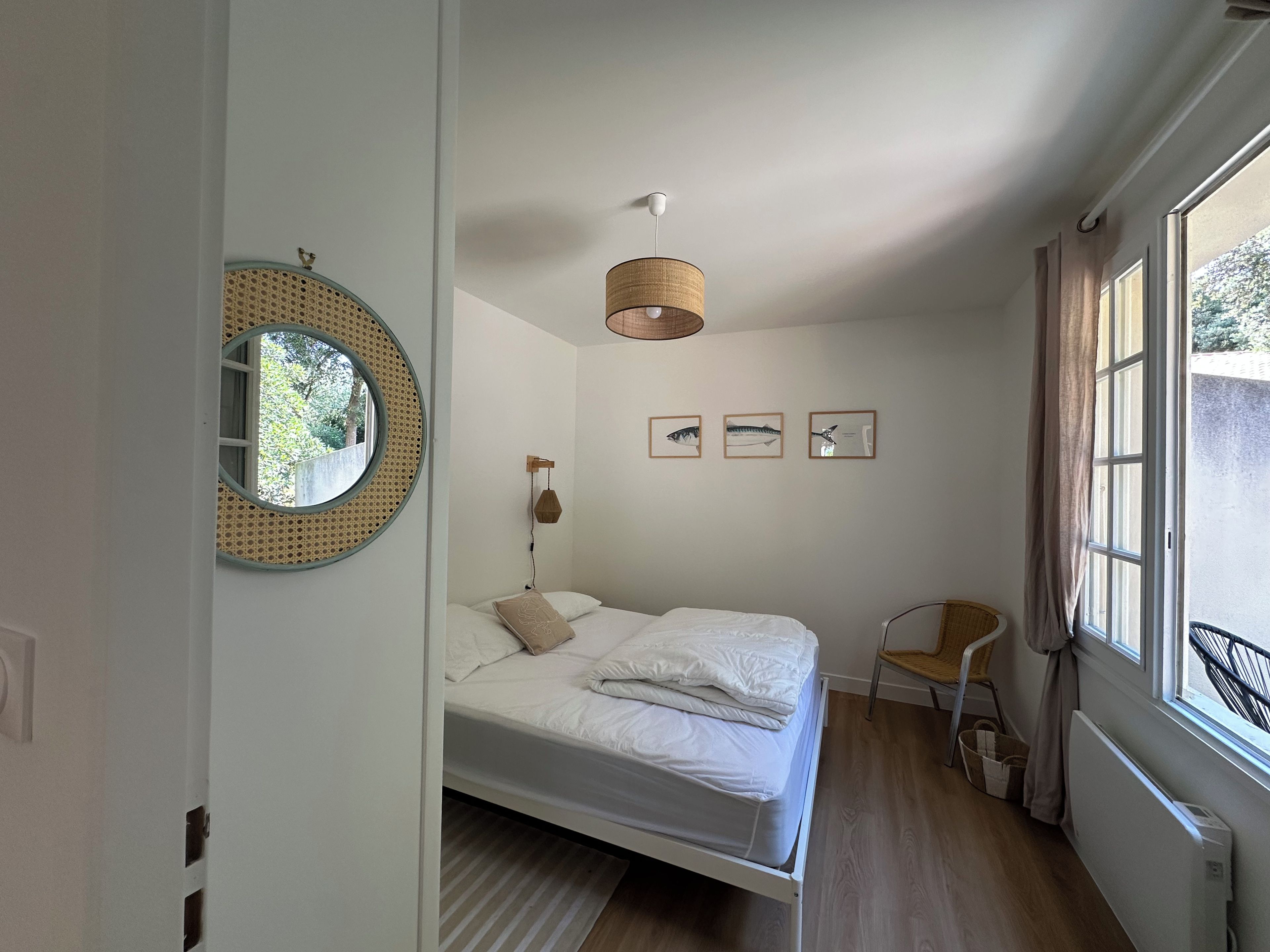 Un dormitorio con una cama, un espejo redondo, una lámpara colgante y cuadros en la pared.