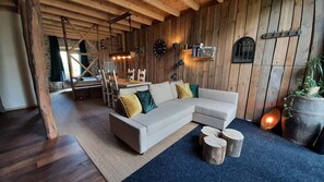 Ein gemütliches Wohnzimmer mit einer Eckcouch, Holzbalken, einer Uhr und rustikalem Flair.
