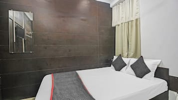 A hotel room with a bed, a mirror, a window with curtains, and a wall with a dark finish.