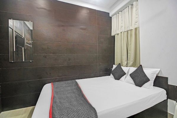 Une chambre d’hôtel avec un lit, un miroir, une fenêtre avec des rideaux et un mur à la finition sombre.