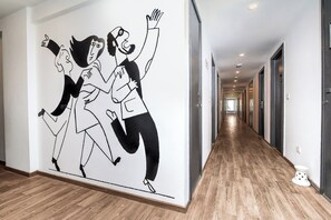 Un couloir orné d’une fresque murale représentant des figures dansantes, doté d’un plancher en bois et de portes donnant accès aux différentes pièces.