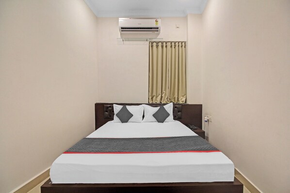A hotel room with a bed, a nightstand, a wall-mounted air conditioner, and a window with curtains. - Townhouse Centre Point Inn Near (Kolkata)