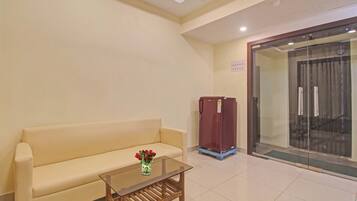 Habitación de hotel con sofá color beige, una mesita de vidrio con un jarrón de flores, un mueble rojo y un vidrio que da a un balcón.