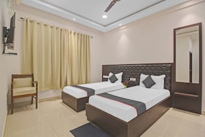 A hotel room with two beds, a chair, a mirror, and a ceiling fan.