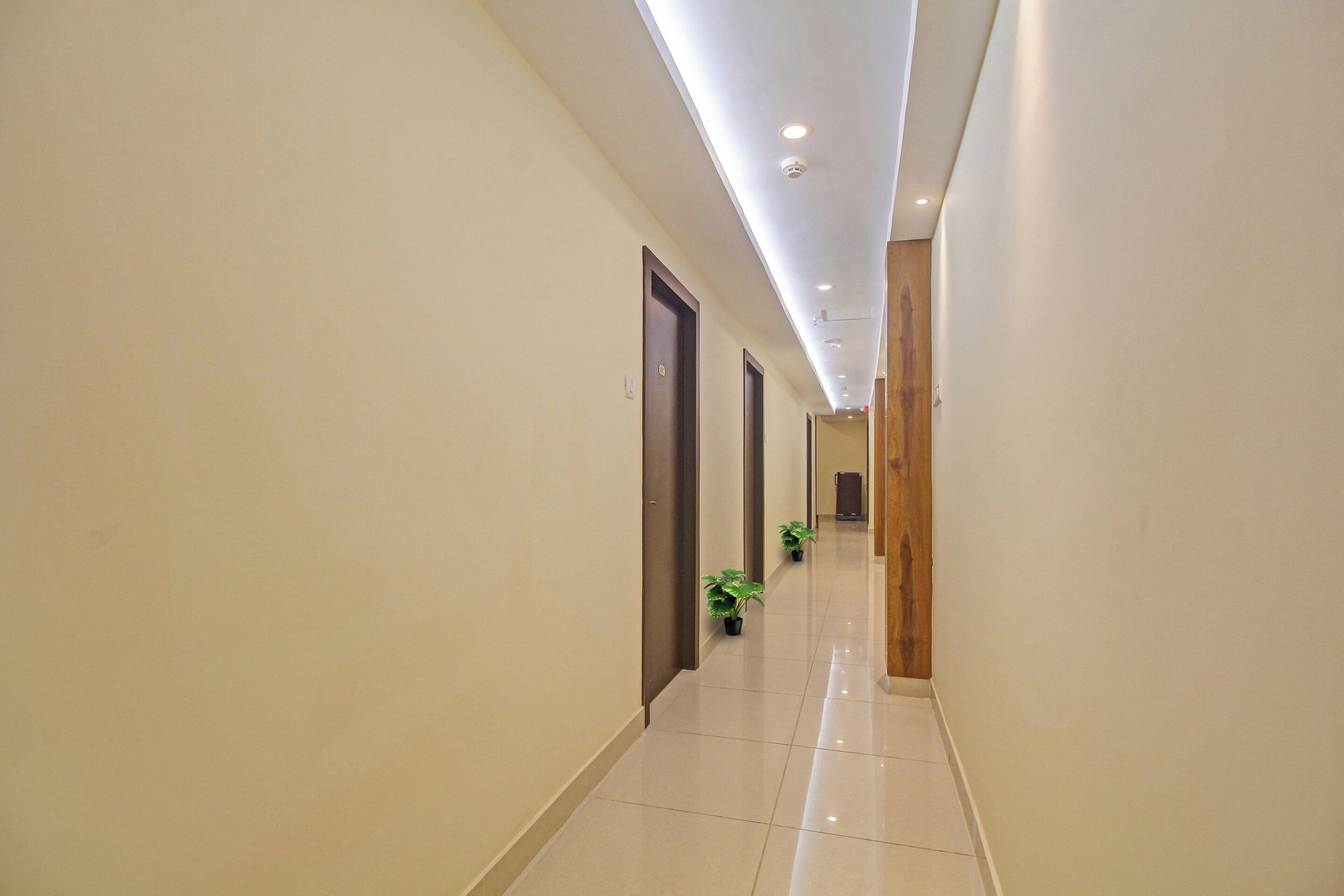 Un pasillo de hotel con piso de baldosas brillantes, puertas de madera e iluminación empotrada en el techo.