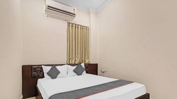 Habitación de hotel con cama, cabecera, ventana con cortinas, unidad de aire acondicionado y un enchufe de pared.