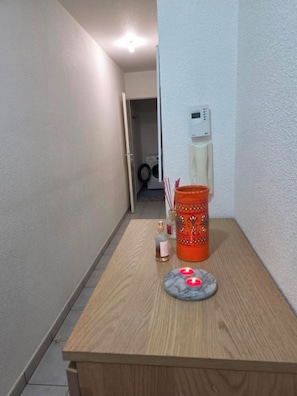 Een smalle gang met een houten tafel, een fles en een decoratieve oranje container.
