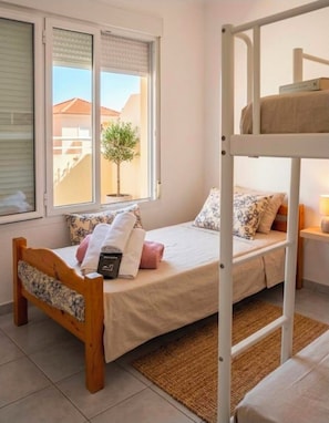Een slaapkamer met een stapelbed, een raam, een kleine potplant en een nachtkastje met een lamp.