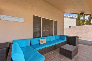 A covered outdoor seating area with a blue sofa and a wicker ottoman. - Amazing Desert Retreat w/Saltwater Pool! (Phoenix)